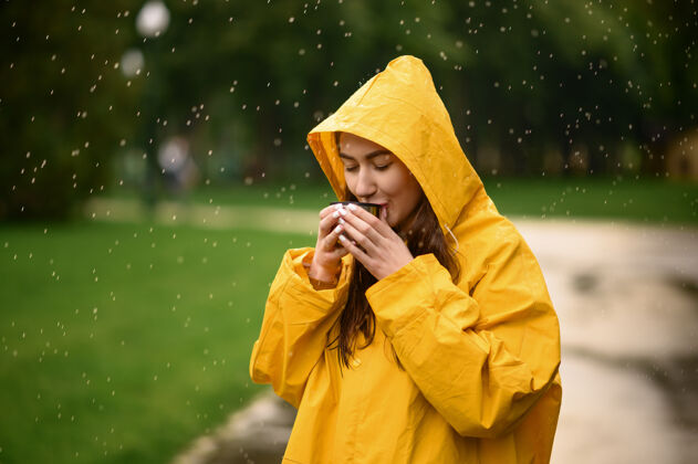 气候雨衣女子在夏日公园喝热茶一天一个人女人穿着雨衣走在小路上 雨天在巷子里保护风景滴