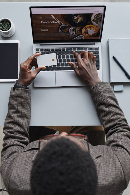 非洲民族非洲商人持有信用卡 使用笔记本电脑在线支付食物的高角度视图室内计算机键盘抱着
