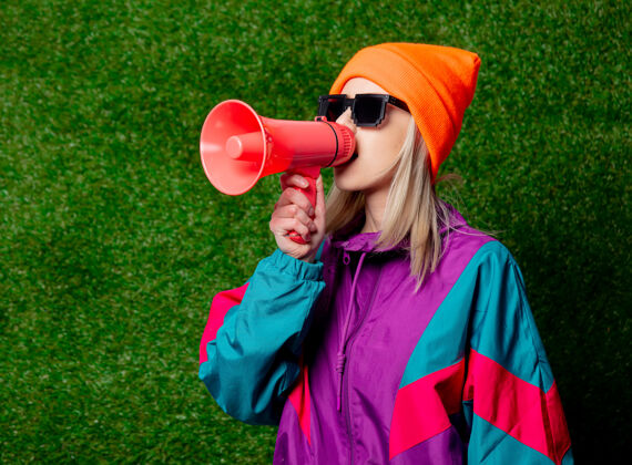 趋势穿着80年代运动服的时尚女孩 绿色草地墙上挂着扩音器时髦草音频