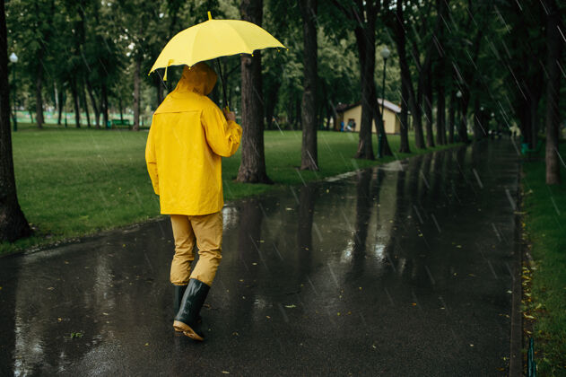 年轻雨中带伞的人在公园散步白天男性穿着雨衣和胶靴的人 巷子里天气潮湿公园白天夏天
