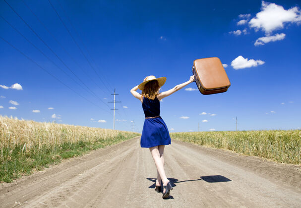 乡村乡间小路上带着手提箱的孤独女孩风包红发