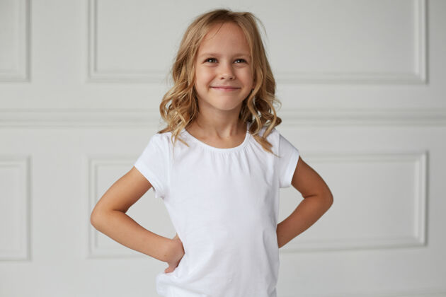 姿势正面肖像是一个小女孩微笑着看着镜头 身着白色衣服 双手放在腰上孩子工作室时尚