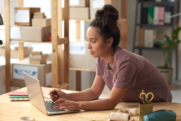 使用计算机在车间桌子旁用笔记本电脑打字的年轻女子上网工作职业