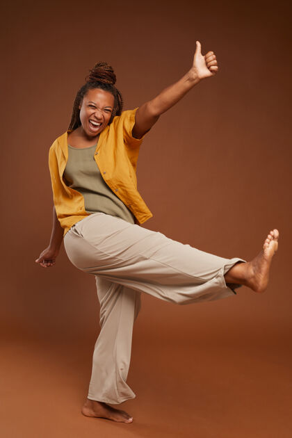 能量在棕色背景下 穿着时髦衣服的兴奋的非洲女人在镜头前摆姿势的肖像自信锻炼舞蹈