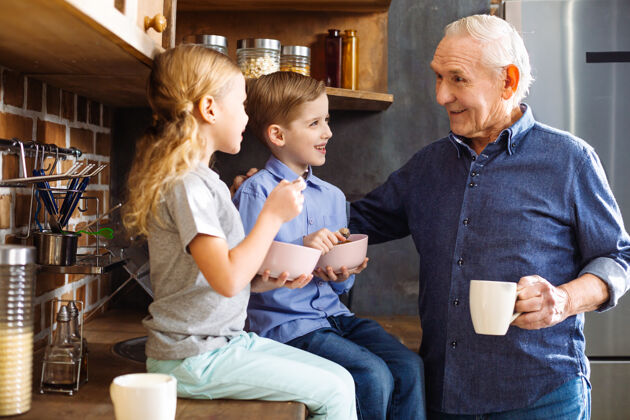 成人快乐微笑的老人一边喝茶 一边享受和孙子孙女们在一起的时光抚养祖父晚餐