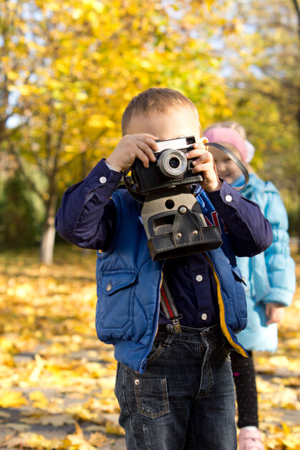 外面一个小男孩拿着一架老式相机 正在扮演一个有抱负的年轻摄影师拍森林小的