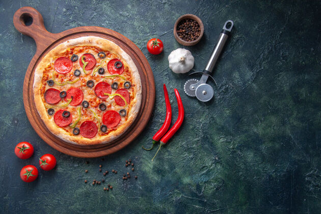 切自制的比萨饼放在木制砧板上 胡椒蒜番茄放在孤立的黑暗表面上橄榄小吃板