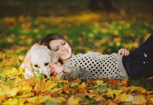 朋友秋天 金发女郎和她的拉布拉多犬躺在公园里的黄叶上温暖友谊叶子