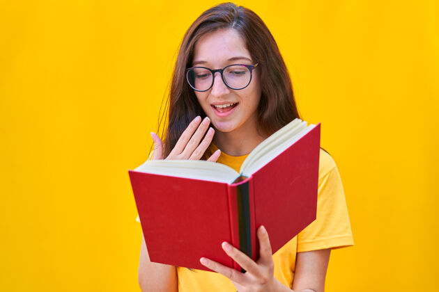 学校一个留着深褐色长发的白人年轻女孩 带着惊讶的表情读着一本红色的书认知书呆子大学