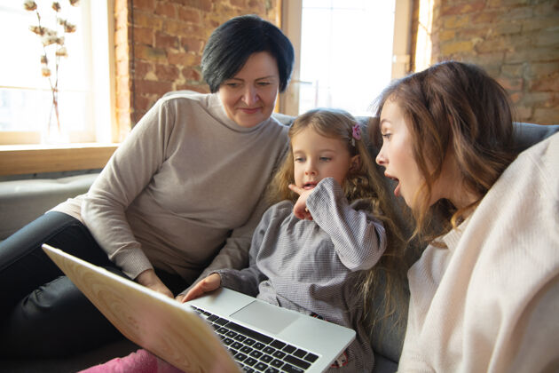 家庭溫暖的心幸福的愛的家庭祖母 母親和女兒一起度過時光看電影 使用筆記本電腦 歡笑母親節 慶祝 周末 假日童年的概念父母臉年輕