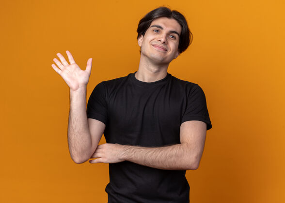 穿着高兴的年轻帅哥穿着黑色t恤 在橙色的墙上显示问候的手势脸年轻市民