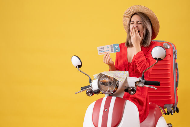 轻便摩托车正面图：穿着红裙子的年轻女士拿着车票 坐在轻便摩托车上打呵欠旅行者游客成人