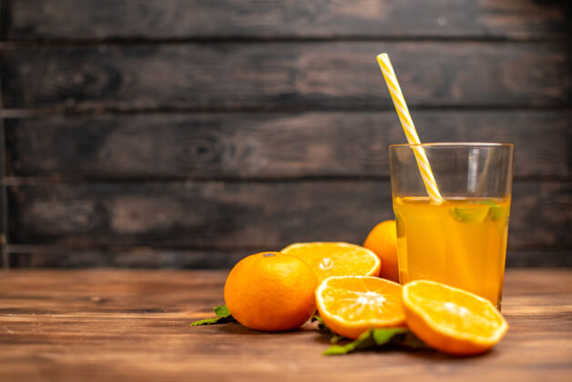 壁板前视图新鲜橙汁在一个玻璃与管薄荷和整个切橙子在左侧的木桌上服务柑橘新鲜