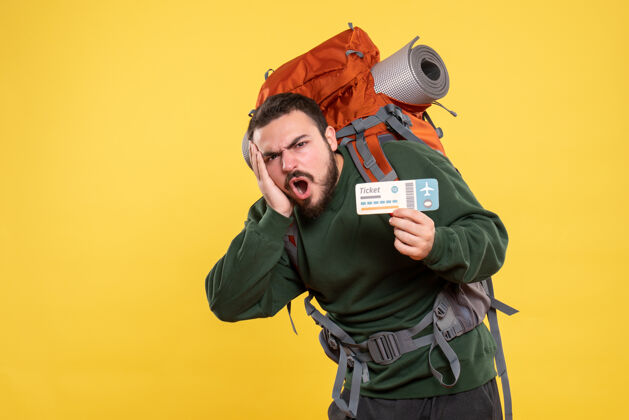 头发情绪紧张的旅行男子背着背包 拿着黄色背景上的票的正面视图人物交流背包