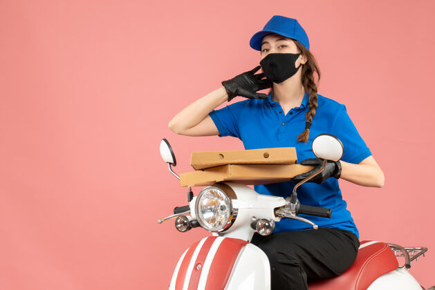 背景年轻的女快递员戴着医用口罩和手套坐在滑板车上传递粉彩桃色背景下的订单前视图手套前面人物