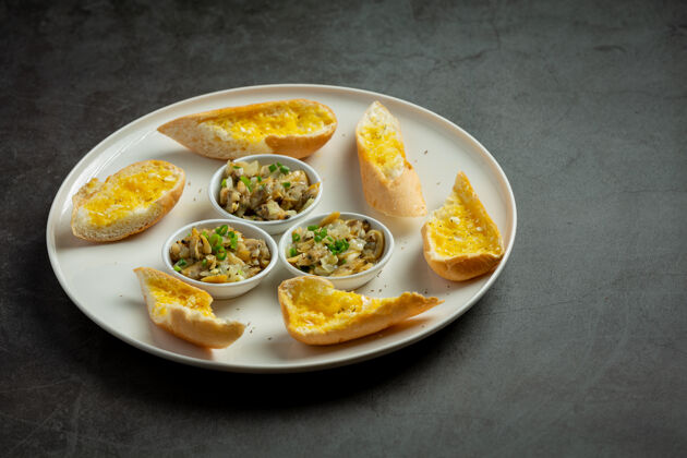 食物烤蛤蜊配大蒜和黄油 配大蒜面包 背景颜色为深色面包一餐白色