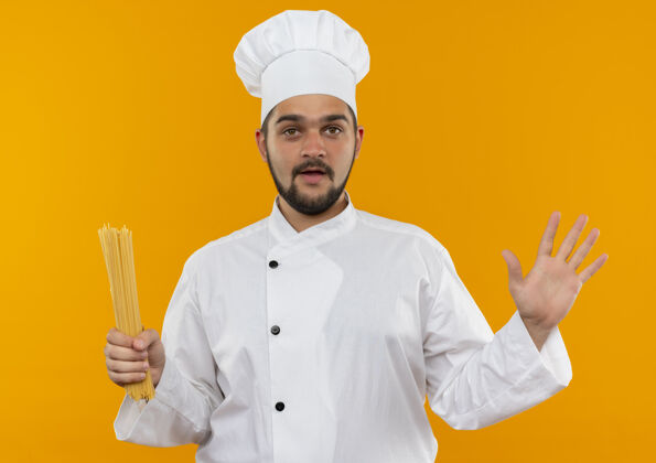 意大利面穿着厨师制服的年轻男厨师手捧意大利面 在橘色的墙上展示着孤立的空手持有空年轻