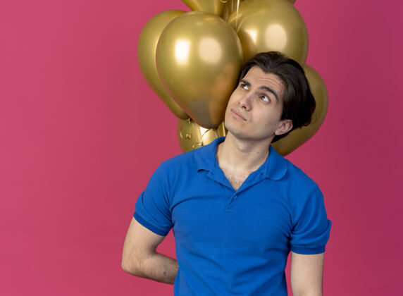 站不知所措的白人帅哥站在氦气球前侧目粉色气球前面