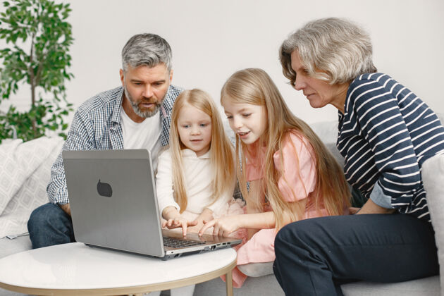 老年人一家人坐在沙发上成熟的男人和女人用笔记本电脑和孙女们玩游戏科技概念打字人家庭