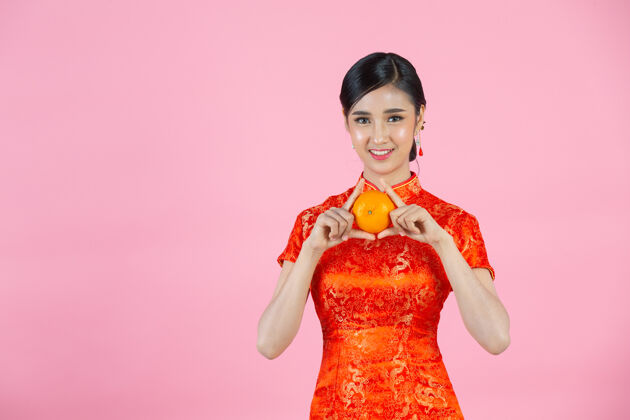 女人美丽的亚洲女人开心地微笑着 手里拿着粉红背景的新鲜橘子过年亚洲年轻演示