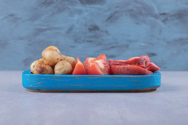 香肠美味的烤香肠和西红柿放在蓝色盘子里辛辣一餐晚餐