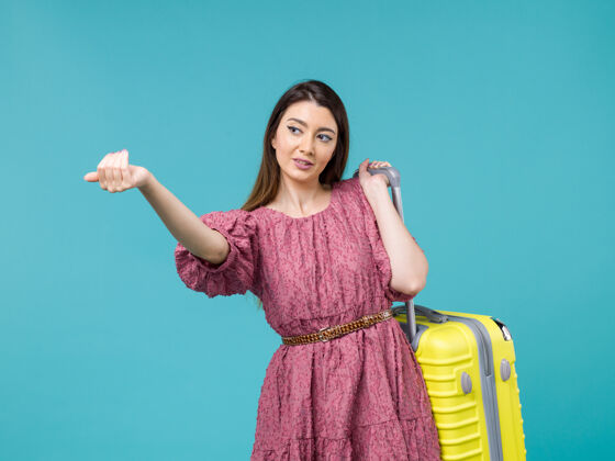 年轻的女人前景年轻女子带着她的黄包去度假浅蓝色背景旅行夏日旅行女人人海旅行衣服包