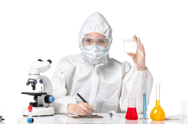 大流行正面图年轻的女医生穿着防护服 戴着口罩 因为拿着一个瓶子 在白色的背景上写着流行的病毒套装防护药品