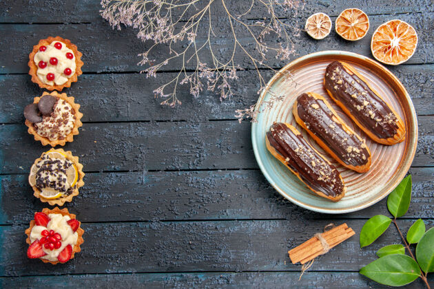 肉桂俯视图：椭圆形平板上的巧克力eclairs干花枝肉桂干橘子叶和垂直排列的馅饼放在黑色木质桌子上 有复制空间食物传统深色