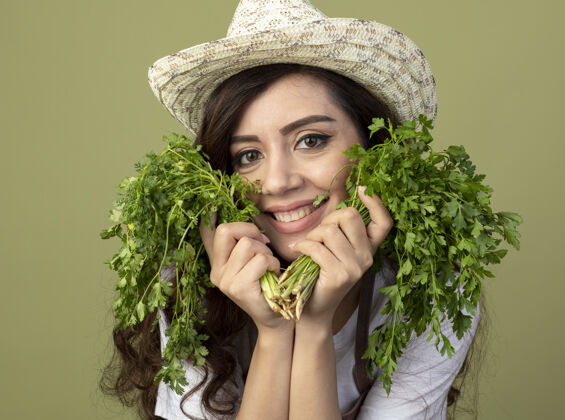 帽子穿着制服的年轻女园丁戴着园艺帽 把香菜放在橄榄绿上女性绿色年轻