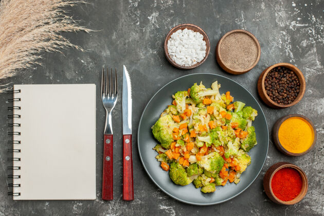 香料健康餐的顶视图 黑色盘子上有花椰菜和胡萝卜 灰色背景上有香料盘子蔬菜背景
