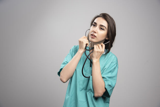 制服身着制服的年轻医生在灰色背景上使用听诊器高质量照片女性健康疾病