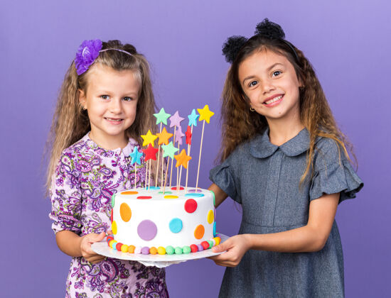 小笑容可掬的小女孩们手拿着生日蛋糕孤零零地站在紫色的墙上 留着复制空间孤立微笑生日