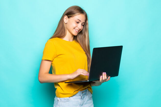 绿松石色在绿松石墙上 一个快乐的年轻女人在笔记本电脑上工作个人电脑时尚年轻人