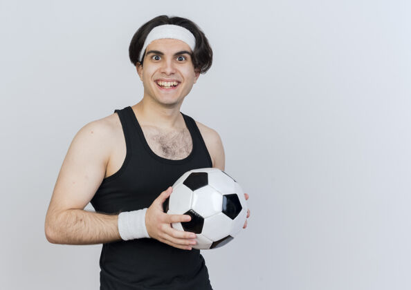 脸身穿运动服 头戴足球带的年轻人站在白色的墙上 面带微笑地看着前方人市民球