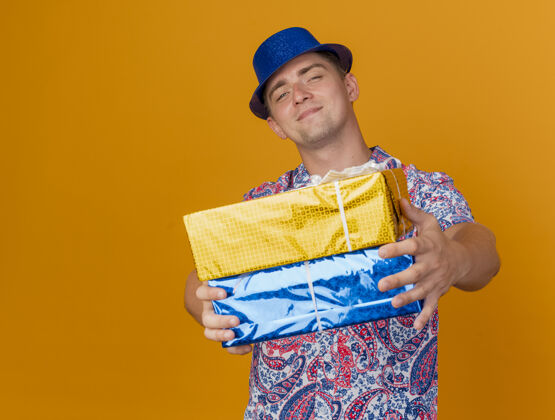 派对高兴的年轻人戴着蓝帽子拿着礼品盒孤立的橙色男人戴着礼物