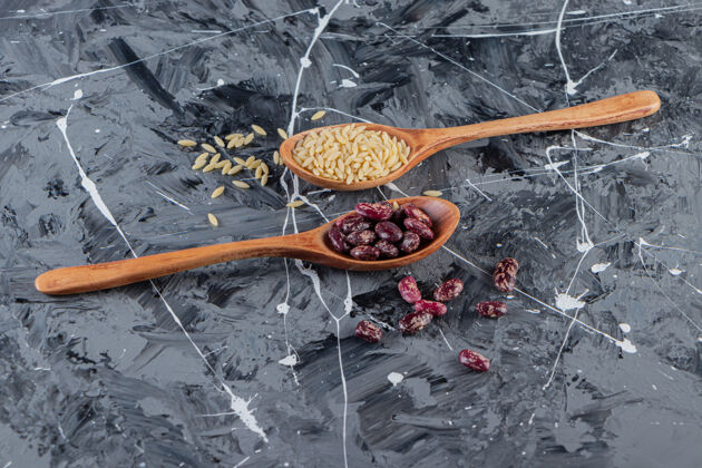 种子在大理石背景上放满了长米饭和豆子的银汤匙豆类营养谷类