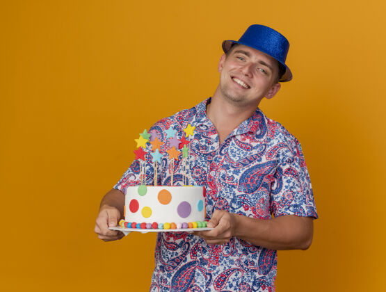 蛋糕微笑着的年轻人戴着蓝色的帽子拿着蛋糕孤立在橙色帽子橙色年轻人