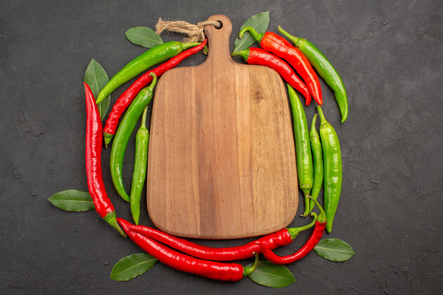 厨房俯视图：红 绿辣椒圈中的砧板和黑色背景上的树叶蔬菜新鲜烹饪