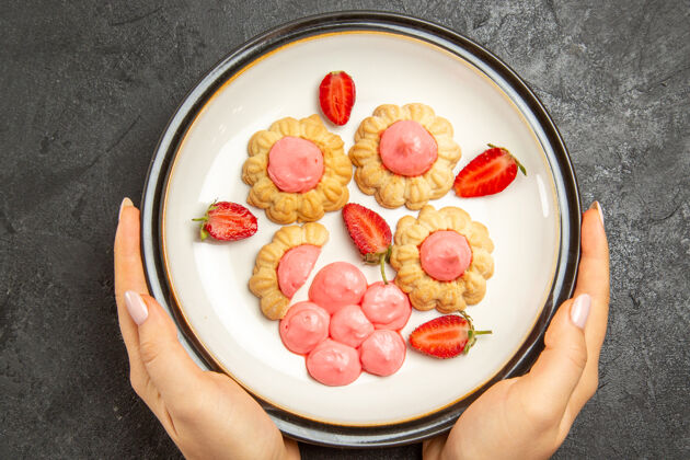 糖在深灰色表面的盘子里有粉红色奶油的美味小饼干俯视图新鲜蔬菜水果