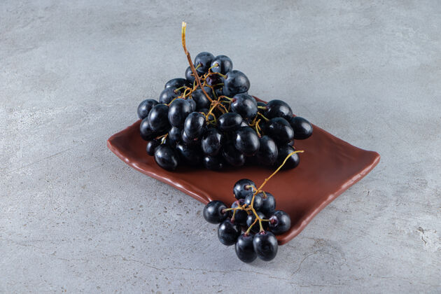 可口在石头背景上放着一盘新鲜的黑葡萄葡萄美味多汁