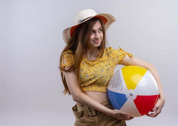 穿高兴的年轻女孩戴着帽子拿着沙滩球 看着右边的空白处和空白处隔离开来女孩拿着帽子