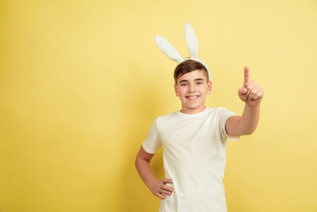 庆祝指着 选择你白人男孩作为复活节兔子在黄色工作室背景复活节快乐的问候美丽的男模人类情感的概念 面部表情 节日复制空间兔子惊喜耳朵