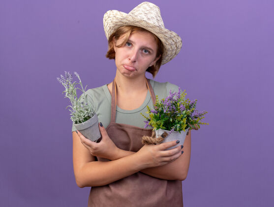 年轻悲伤的年轻斯拉夫女园丁戴着园艺帽拿着紫色花盆里的花花园园艺花盆