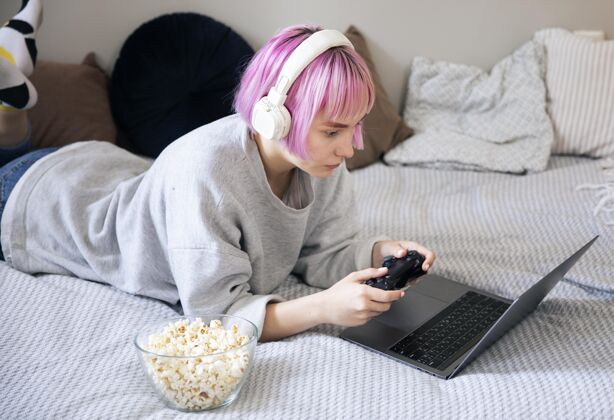 玩家粉红色头发的年轻女子在玩笔记本电脑上的操纵杆享受女人室内
