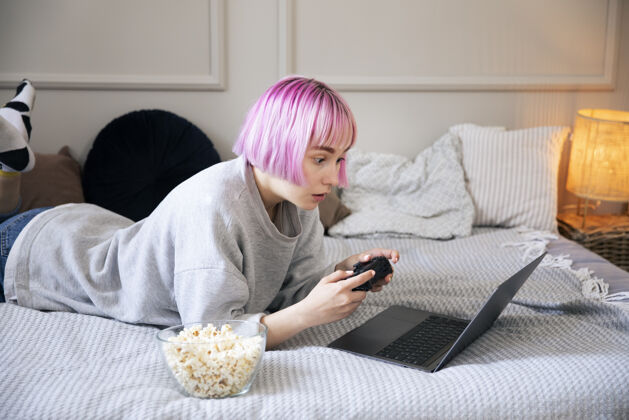 玩家粉红色头发的年轻女子在玩笔记本电脑上的操纵杆虚拟女人视频游戏