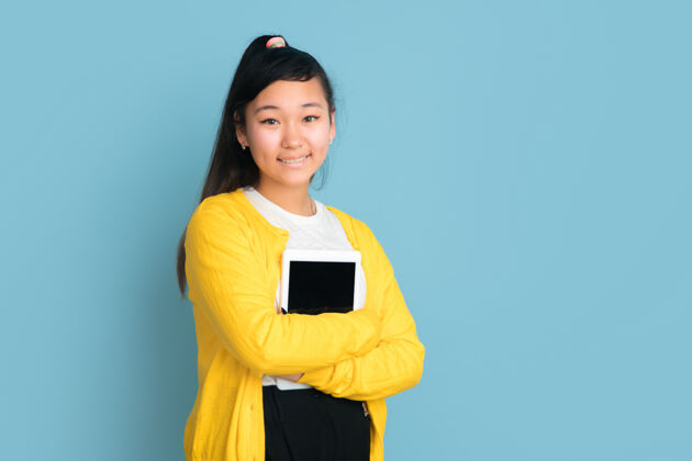工作在蓝色工作室背景上孤立的亚洲青少年肖像美丽的深褐色长发女性模特人类情感的概念 面部表情 销售 广告手持平板电脑 微笑成功主管Vlog