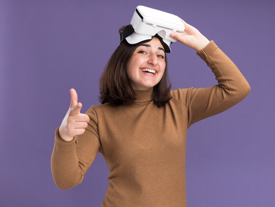 相机带着贝雷帽的年轻漂亮白人女孩微笑着手持vr耳机 指着紫色的相机微笑耳机虚拟现实