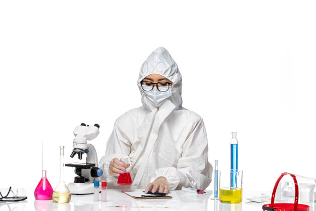 面罩前视图身着特殊防护服的女化学家手持浅白背景上的红色溶液-化学病毒实验室健康专业医学