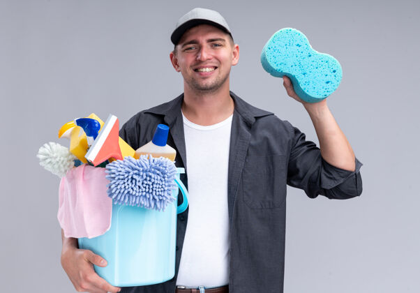 表情面带微笑的年轻帅气的清洁工穿着t恤 戴着帽子 拿着一桶清洁工具和海绵隔离在白色的墙上海绵感觉人