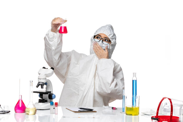 女化学家正面图白色办公桌上穿着特殊防护服的女化学家拿着红色溶液-化学病毒实验室人持有病毒